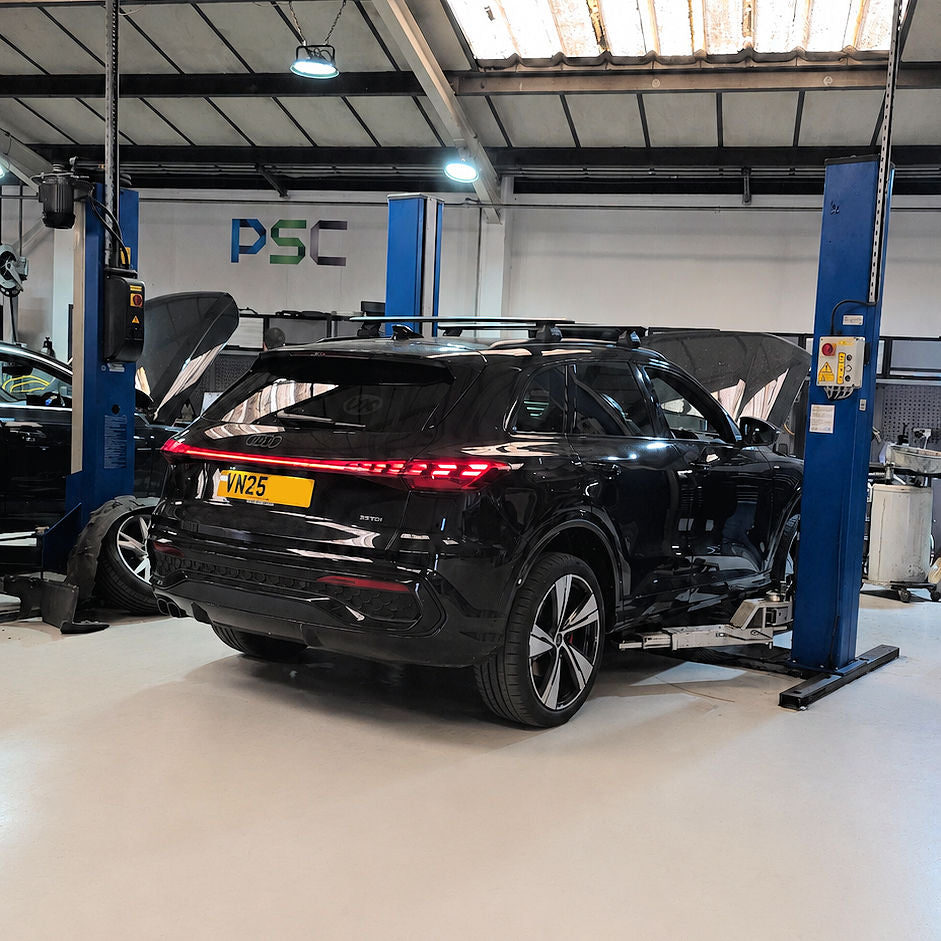 Black Audi Q5 raised on a workshop ramp inside PSC Autocentre, rear view showing illuminated tail lights