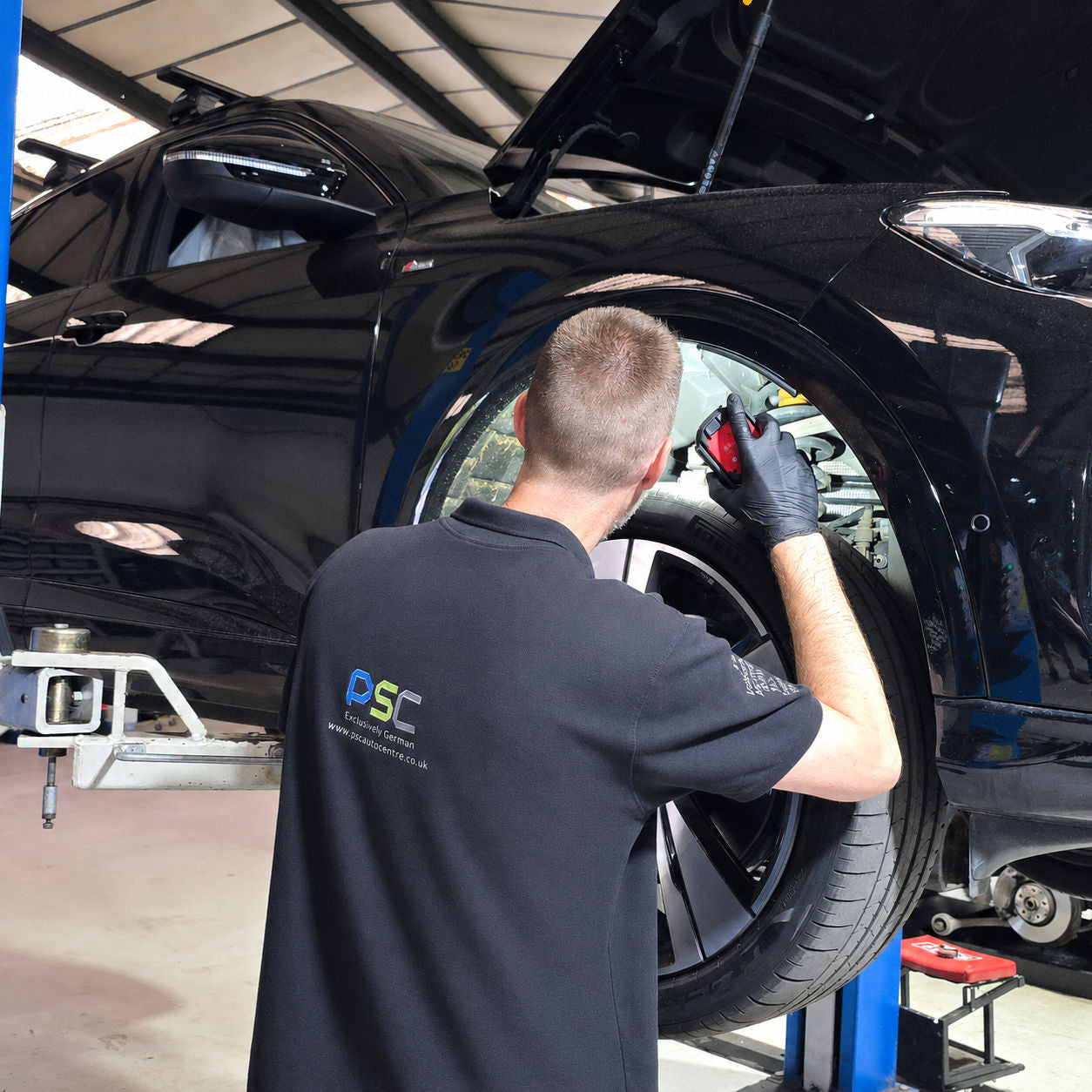 PSC Autocentre technician in branded workwear carrying out inspection work on a black Audi's front wheel arch